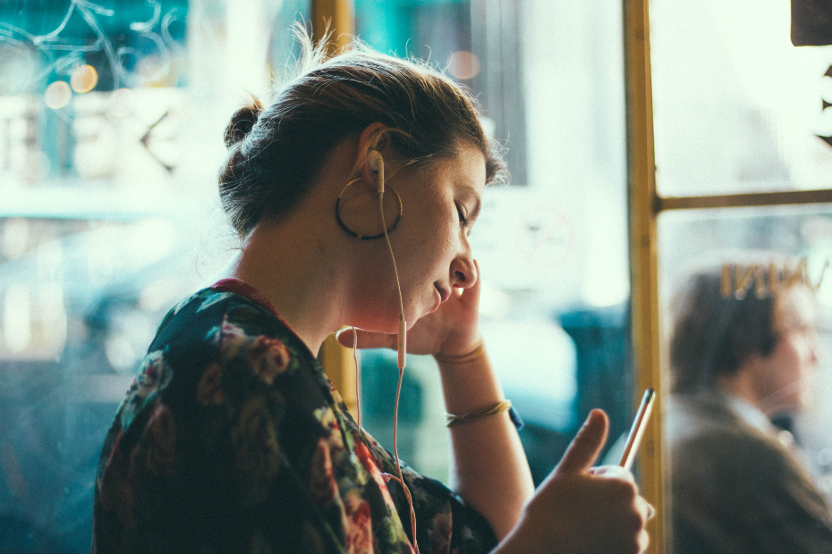 woman with hoop earrings has apple headphones in while she sits casually at a coffee shop, listening to music