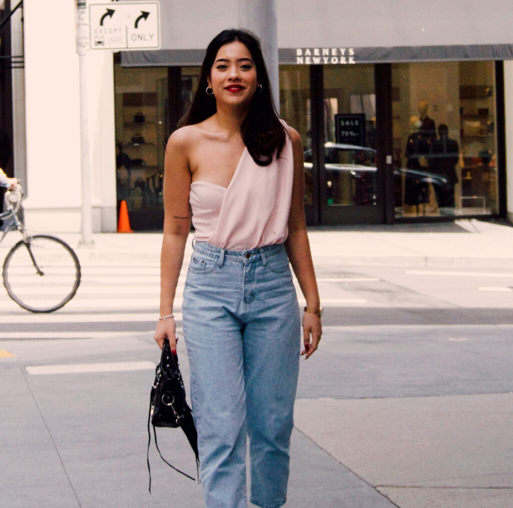 brunette haired girl in baggy light denim jeans walks on street in front of barney's new york