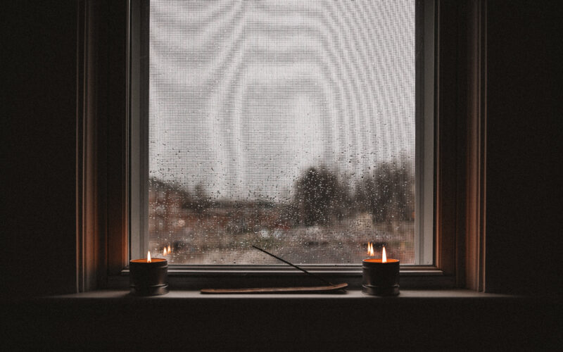candles sit in front of a windowsill on a rainy day likely during winter or fall. calm and mellow