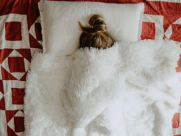 girl with a bun lays in bed with white blanket over her body