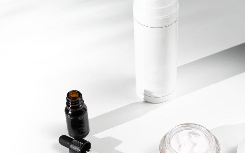 a dropper, serum package and cream or moisturizer sit on a white table
