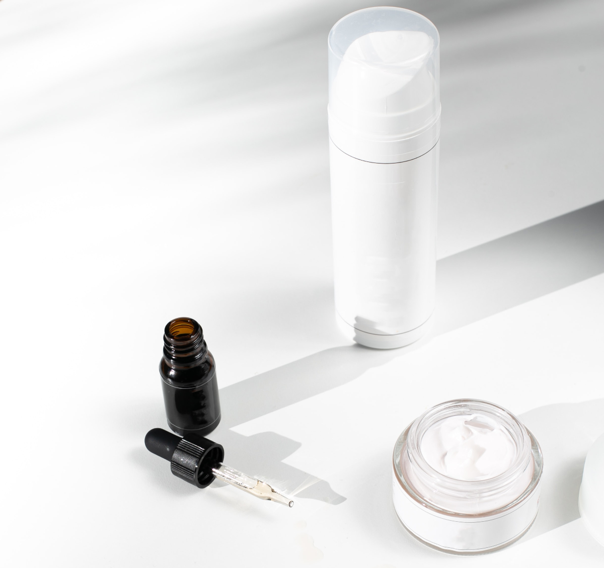 a dropper, serum package and cream or moisturizer sit on a white table