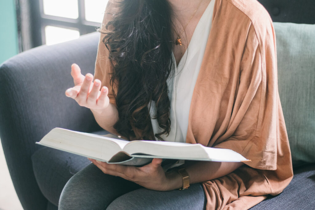 woman with brown hair sits on couch with book