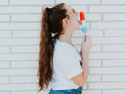 brown haired brunette with long locks licks a red white and blue popsicle wearing a white t-shirt