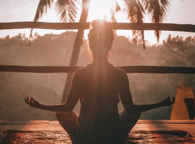 girl meditates on wooden balcony in front of a palm tree during a wellness experience